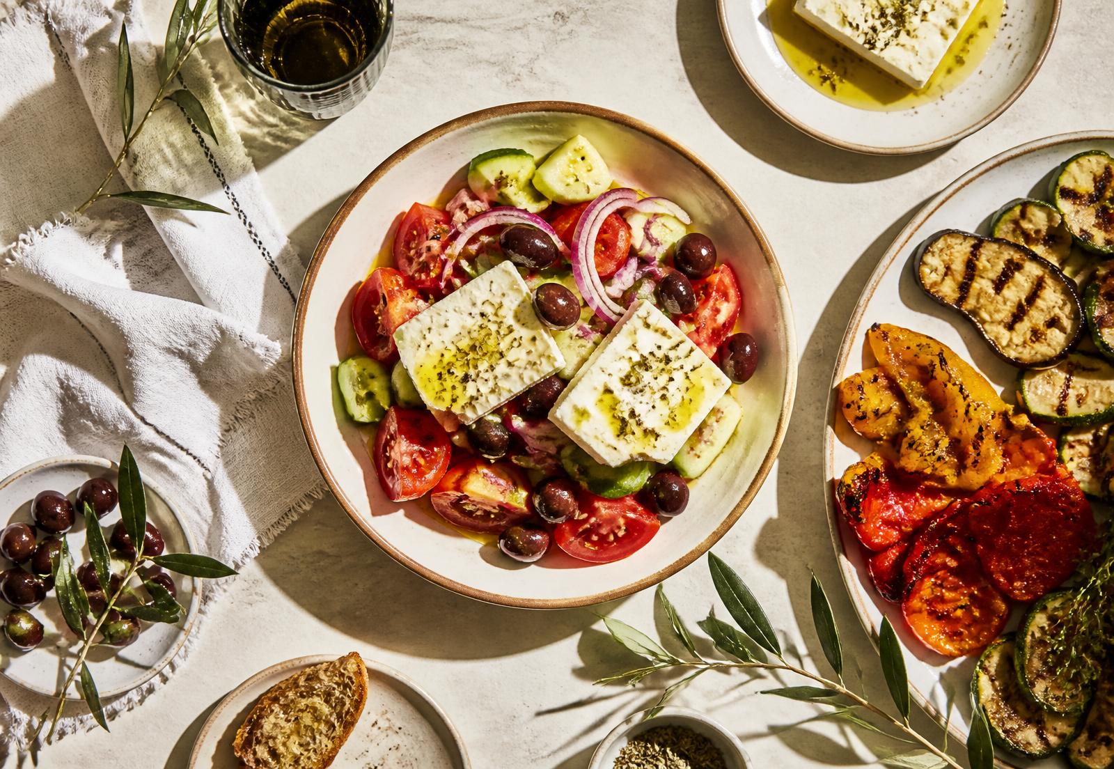 Mediterranean table with Greek salad, grilled vegetables and olive oil in warm sunlight